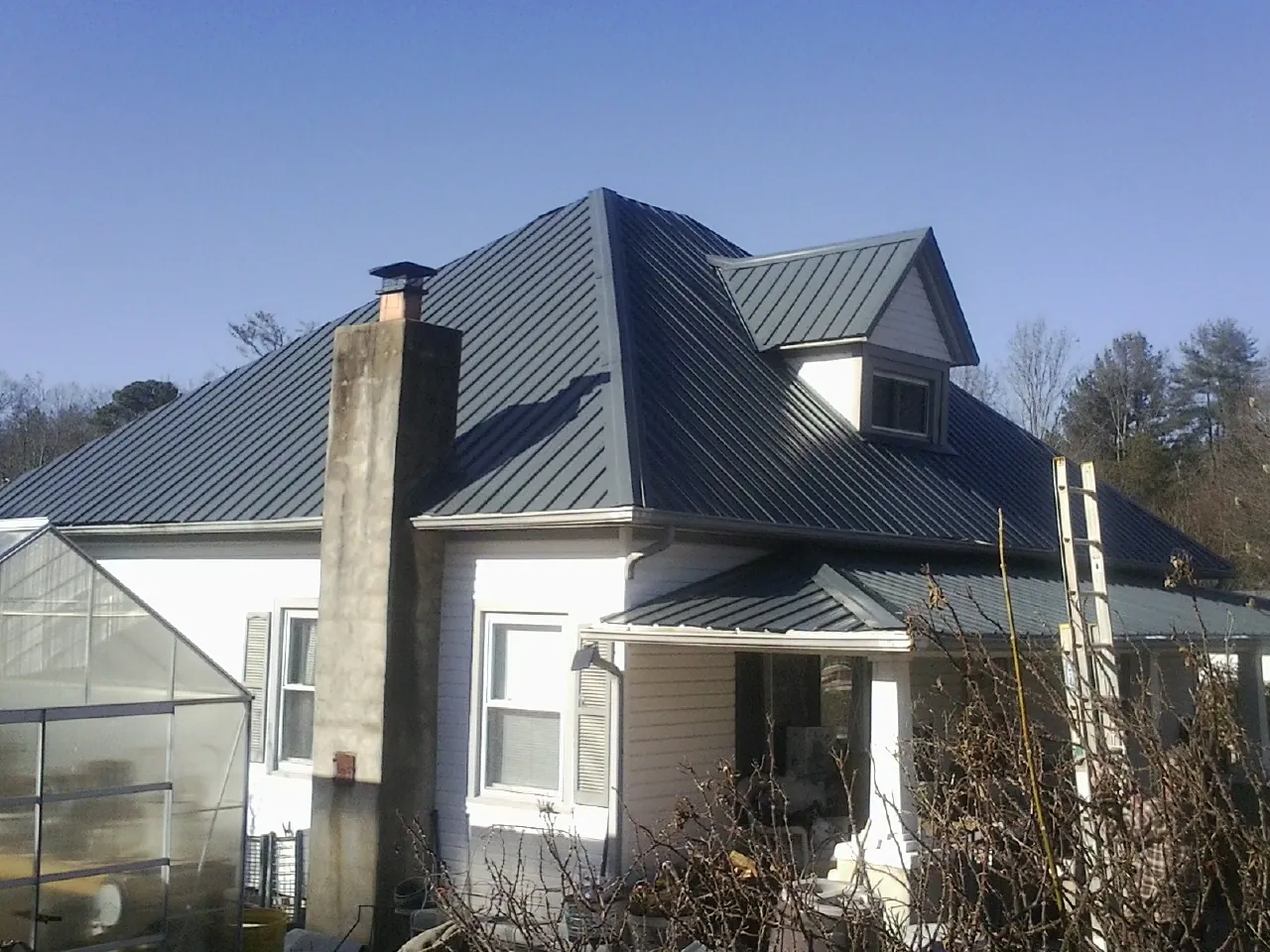 Dark blue standing seam metal roof on a white farmhouse with dormer — Slate & Tile Roof Repair by Roofing Brothers in Trade