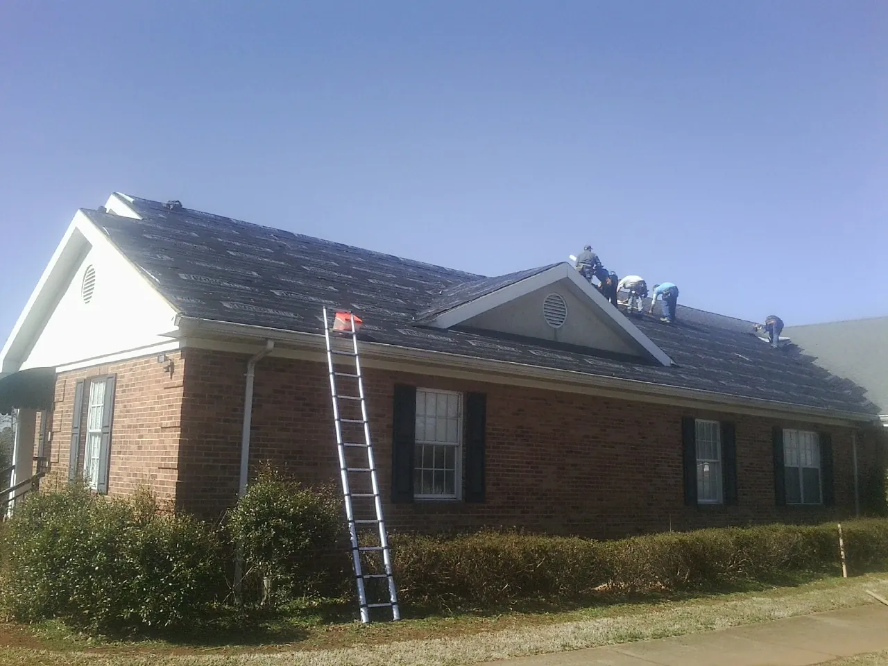 Crew tearing shingles off a brick ranch roof with a ladder set — Metal Roof Repair work by our crew in Trade