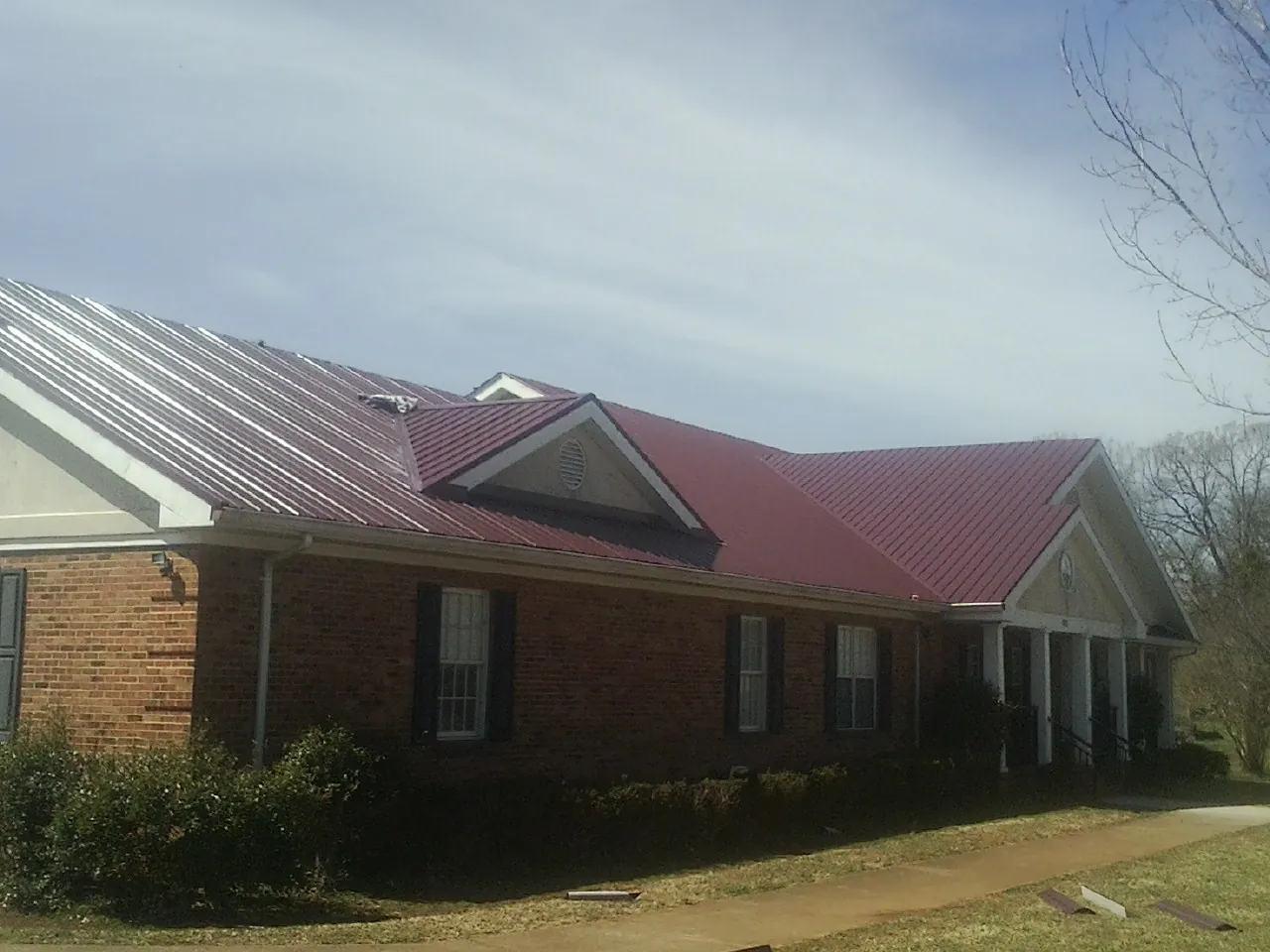 Red metal roof with gabled entries on a long brick building, from a Hail Damage Roof Repair job in Trade