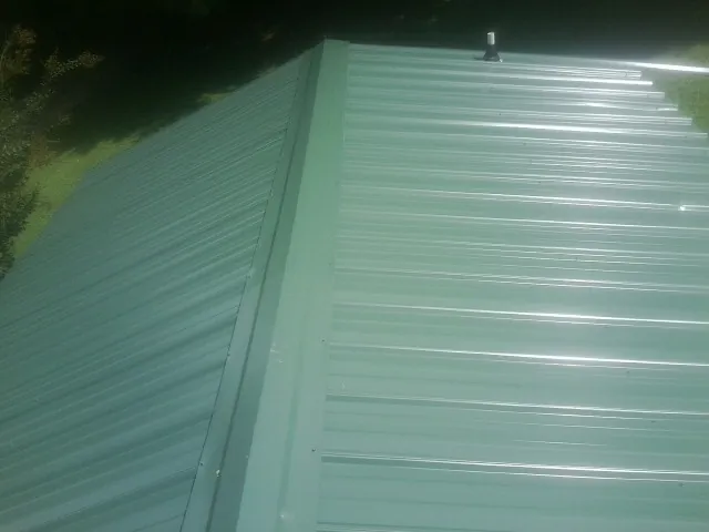 New green metal panels meeting at the ridge of a roof — Flat Roof Repair work by our crew in Trade