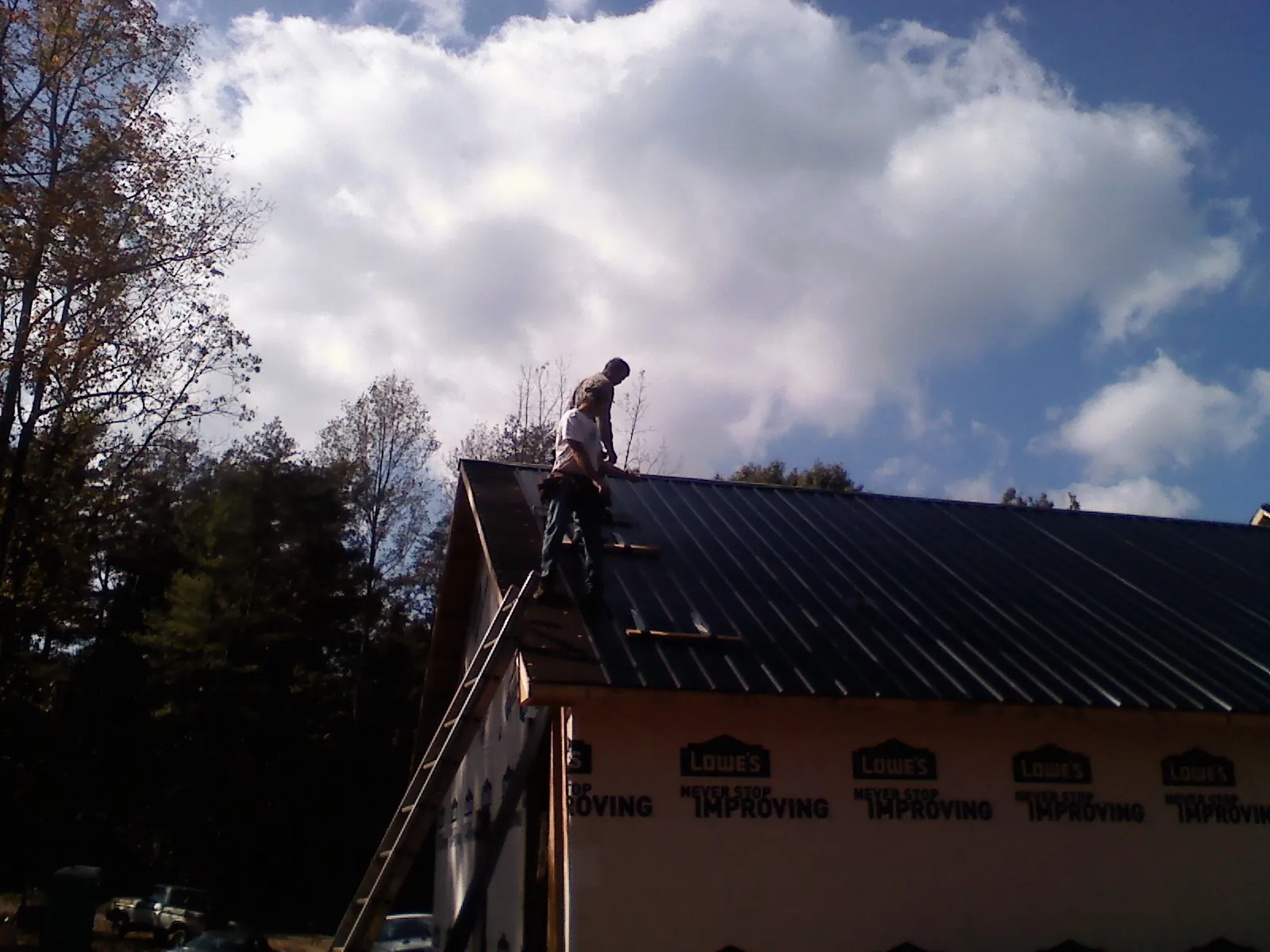 Roofer fastening dark metal panels high against a cloudy sky, from a Roof Inspection job in Trade