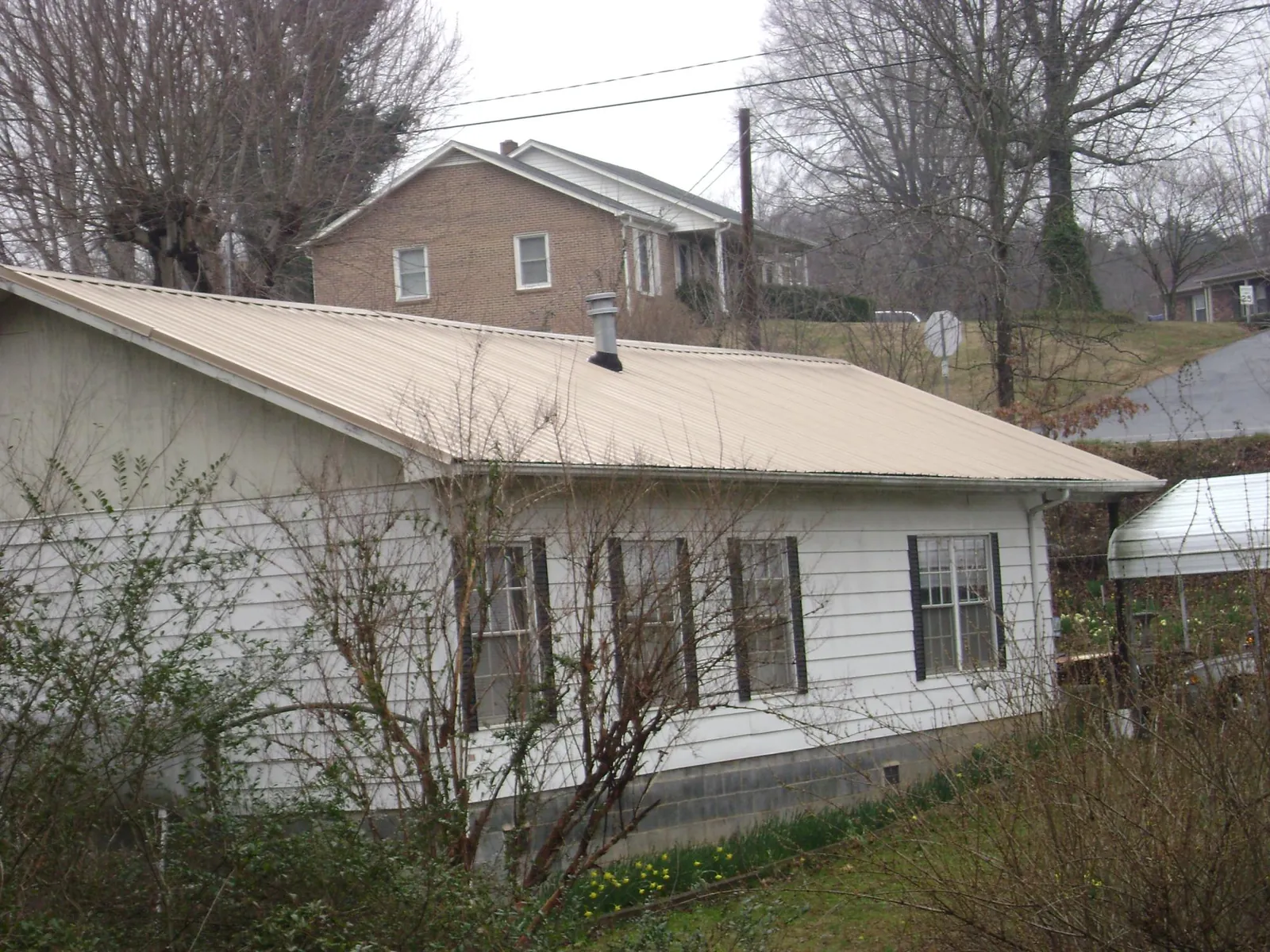 Tan metal roof on a white sided house set into a hillside — Commercial Roofing by Roofing Brothers in Trade