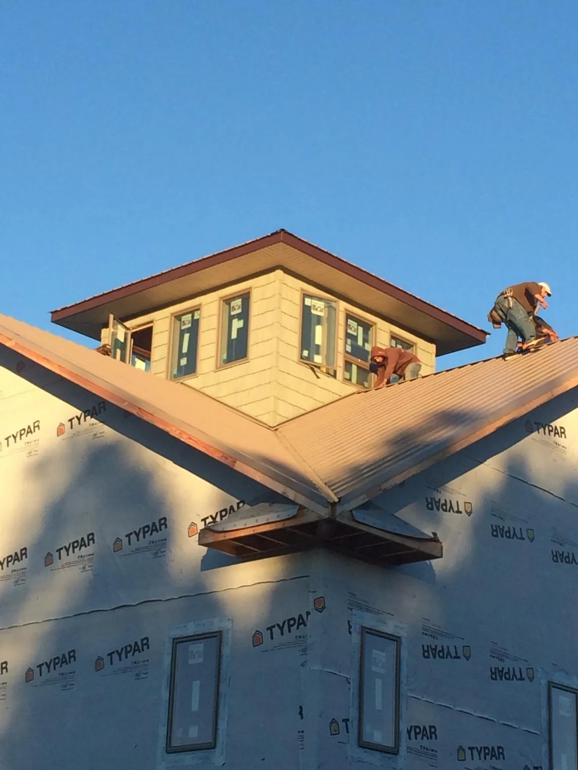 Roofers working around a rooftop cupola on a new metal roof at sunset — Roof Waterproofing in Trade by Roofing Brothers